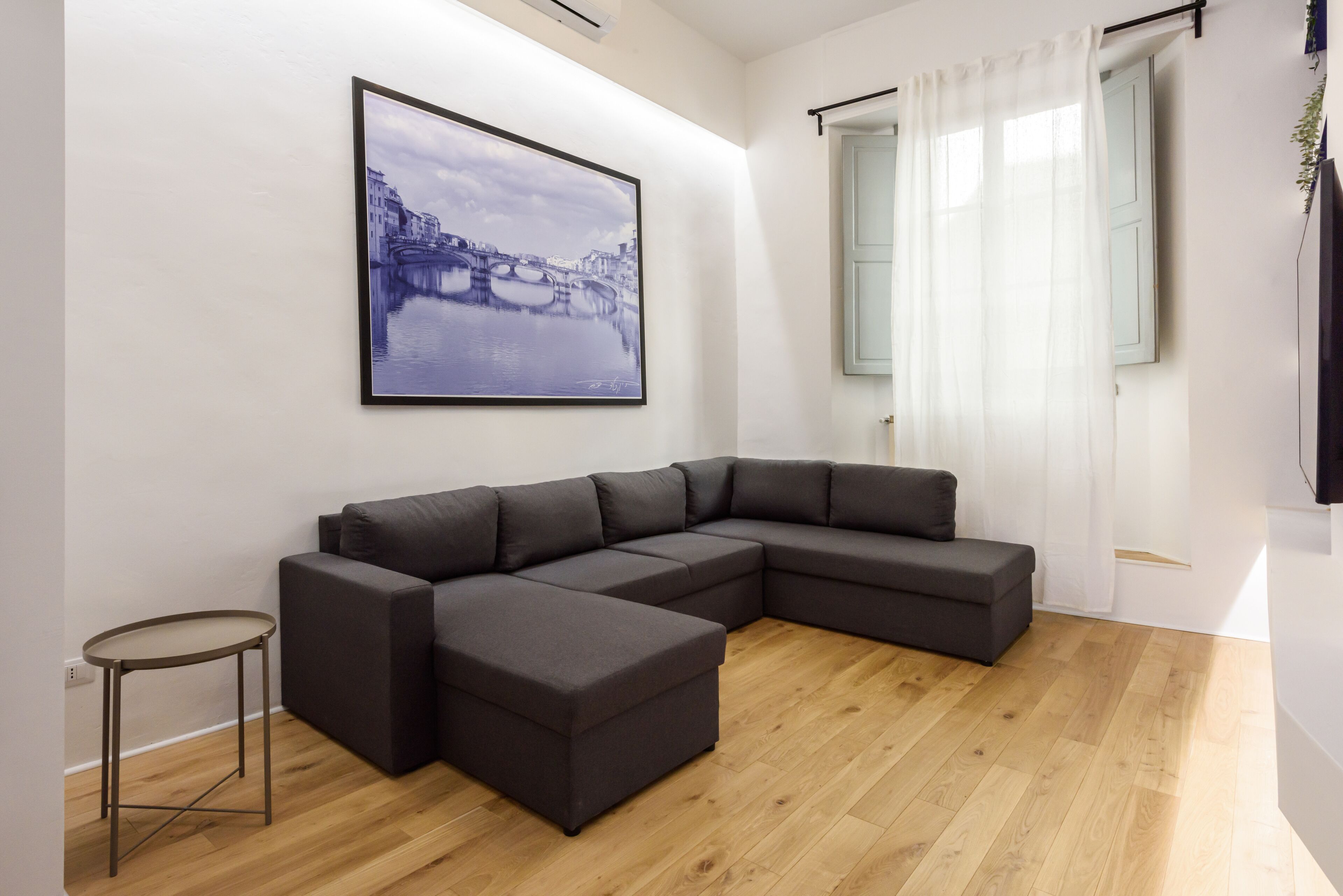 A modern living room with a sectional sofa, a small side table, and a framed cityscape picture on the wall.