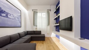 Un salon moderne avec un canapé d’angle, un téléviseur à écran plat fixé à un mur blanc et un plancher en bois.
