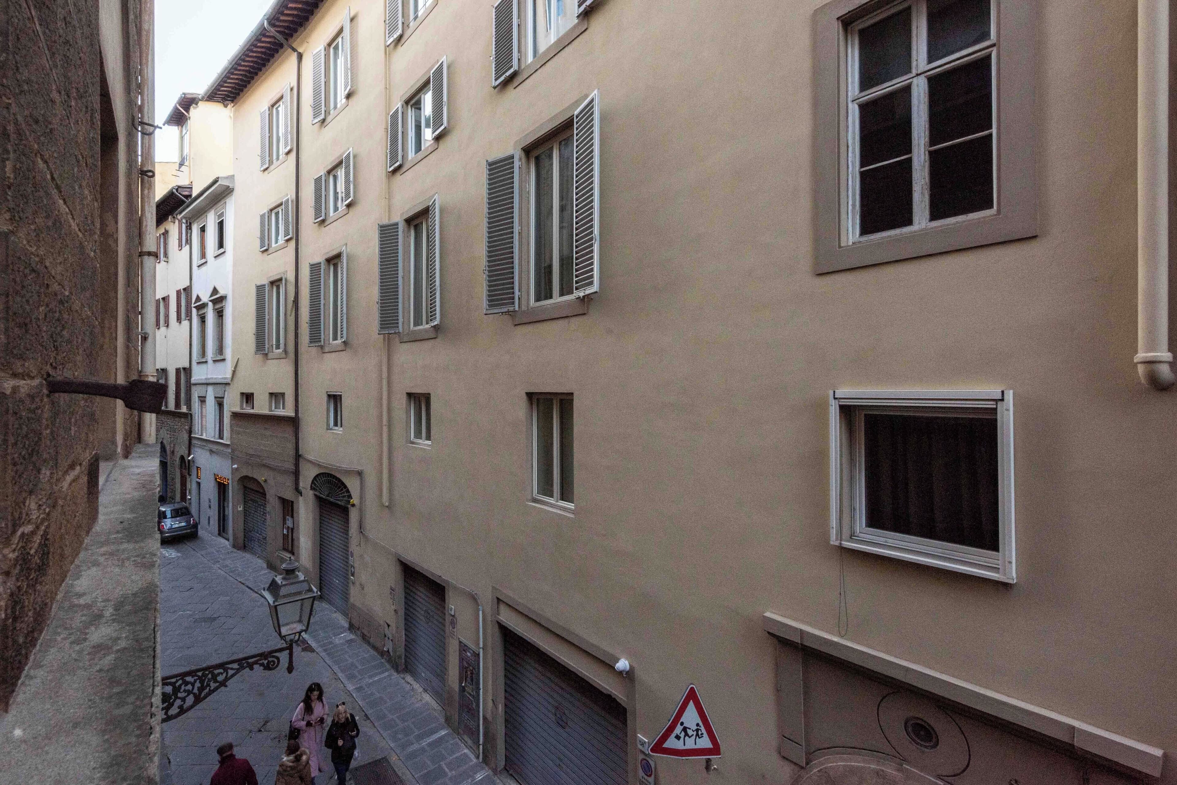 A narrow street with buildings on both sides, featuring multiple windows and shutters.