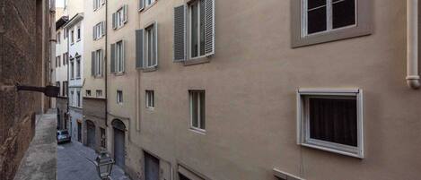 A narrow street with buildings on both sides, featuring multiple windows and shutters.