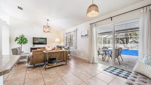 A modern living room with a TV, sofa, dining area, and a view of a swimming pool. - Entire home, Heated Pool, Lake view and Gazebo! (Riverview)