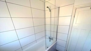 Een badkamer met witte betegelde wanden, een douchecabine met glazen wanden en een bad.