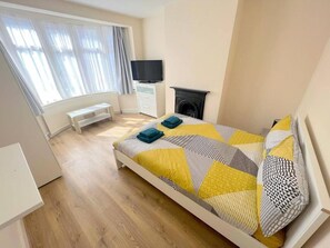 Ein Schlafzimmer mit einem Bett, einem Fernseher, einem Kamin und einem Fenster mit Vorhängen.