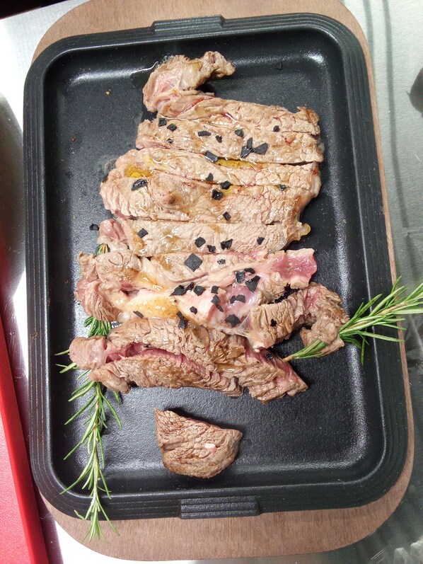A black tray with sliced meat and rosemary on a wooden surface. - Tenuta Torre Diana (Mordano)