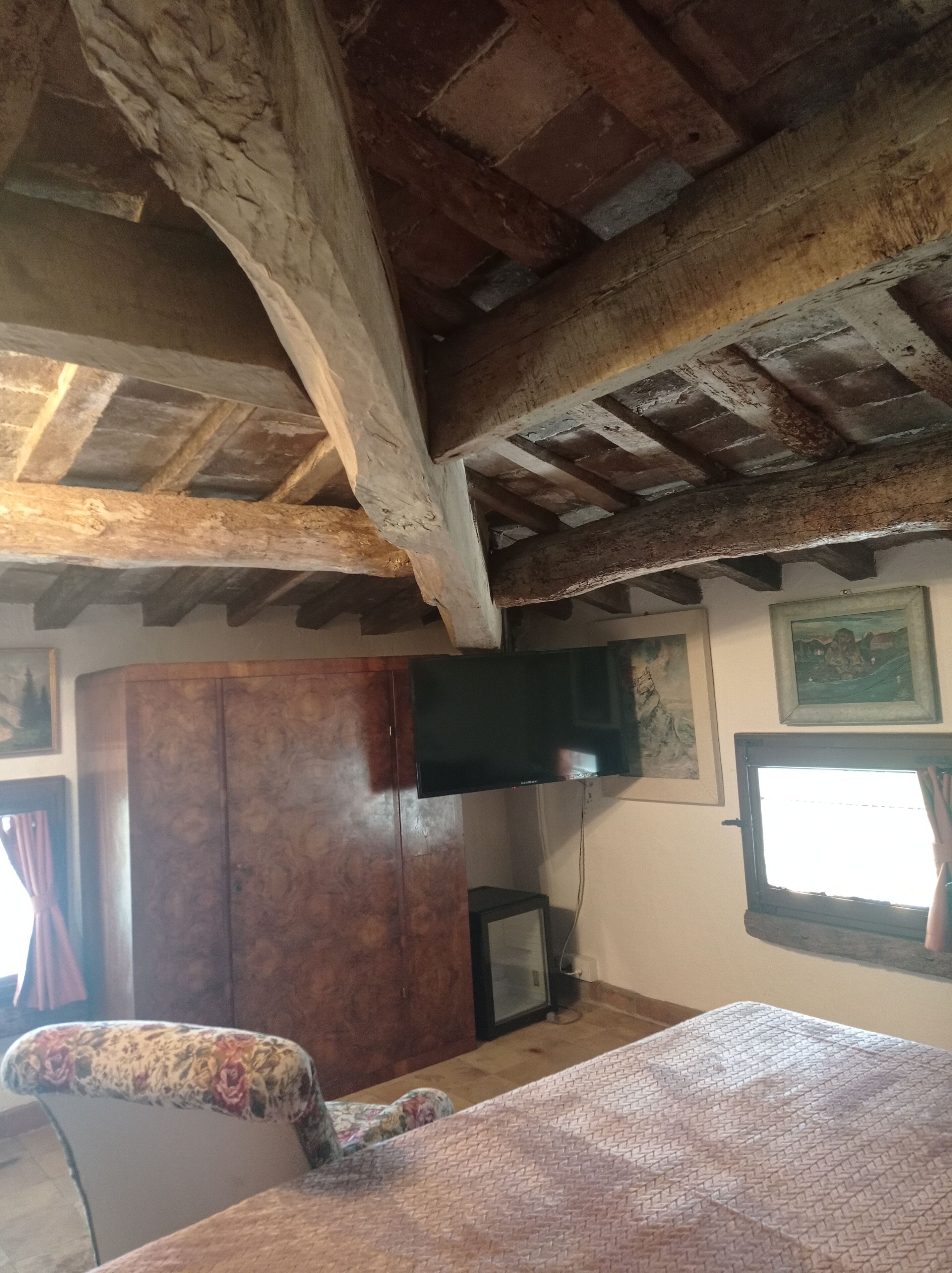 A rustic room with exposed wooden beams, a television, a cabinet, and a bed.