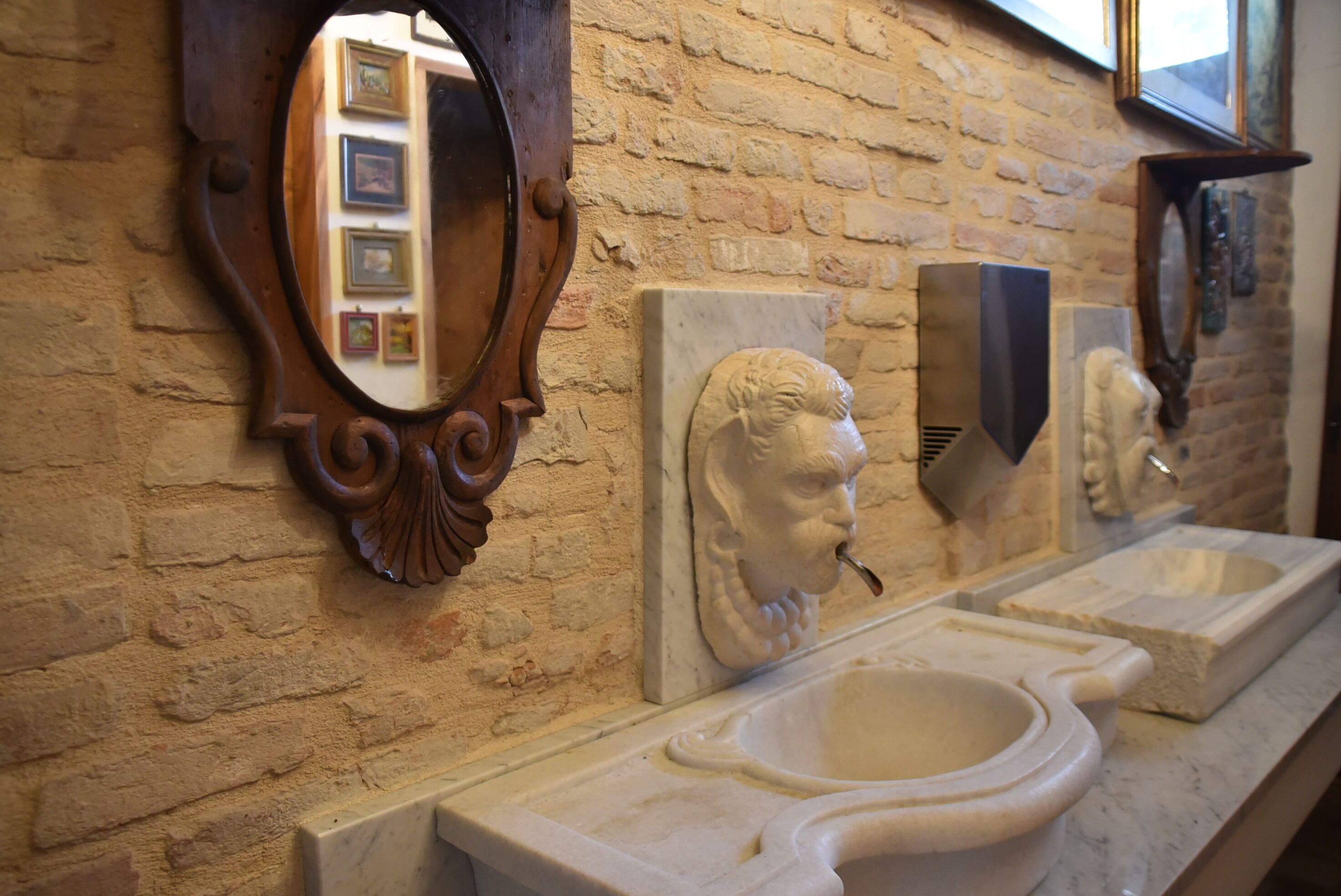 A bathroom with a brick wall, a wooden-framed mirror, and a marble sink.