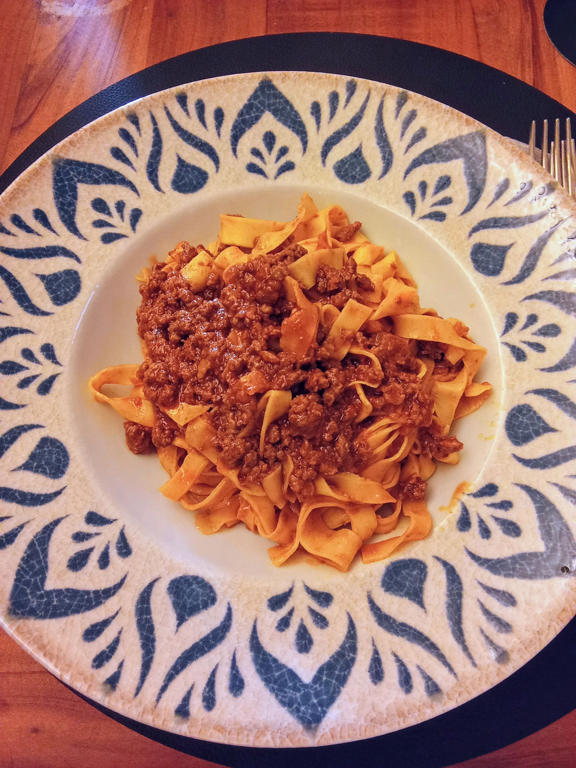 A plate of fettuccine with a meat sauce, served on a decorative plate with a blue and white pattern.