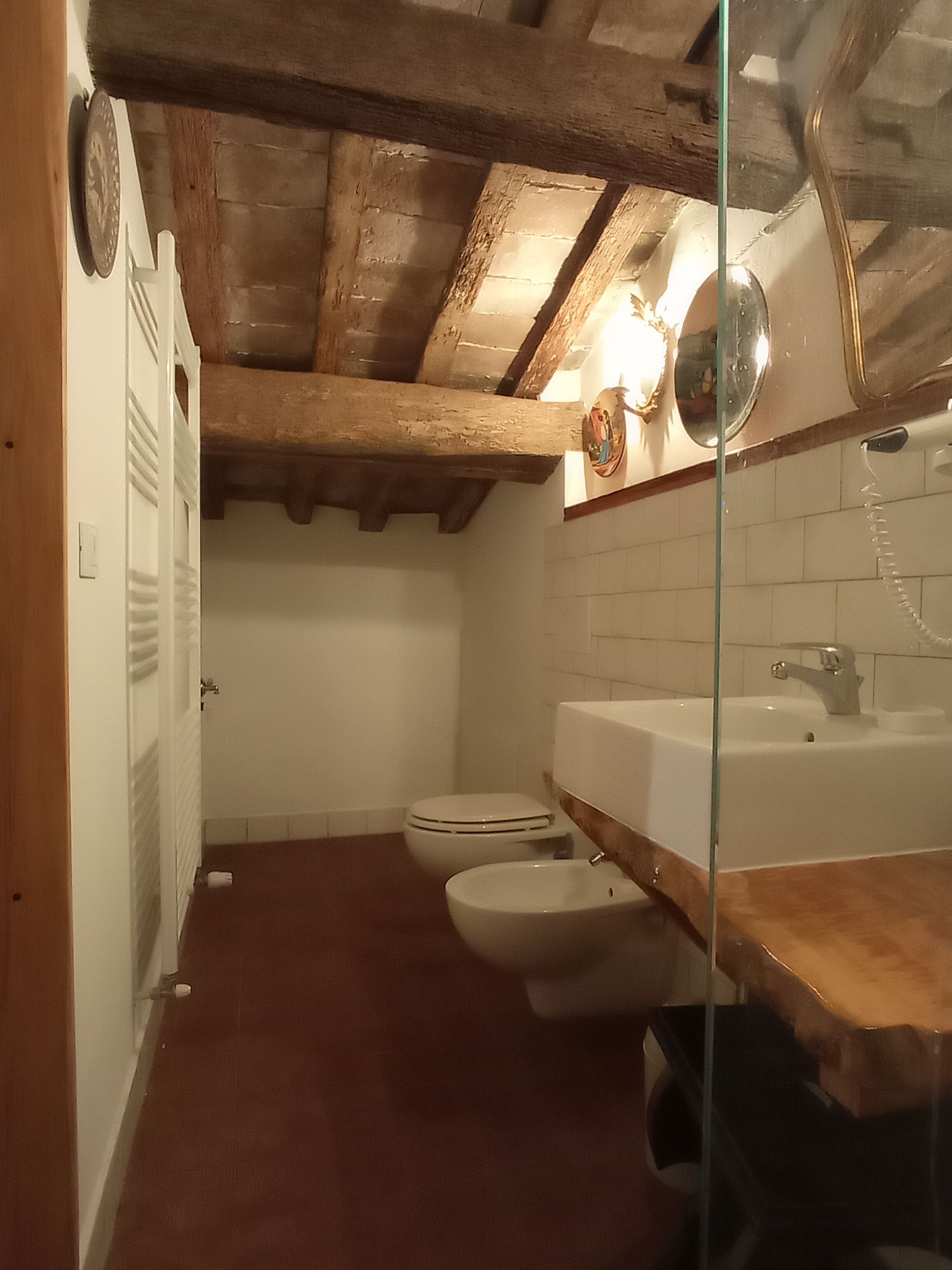 Ein Badezimmer mit Holzboden, einer weißen Toilette, einem weißen Waschbecken und einem Spiegel.