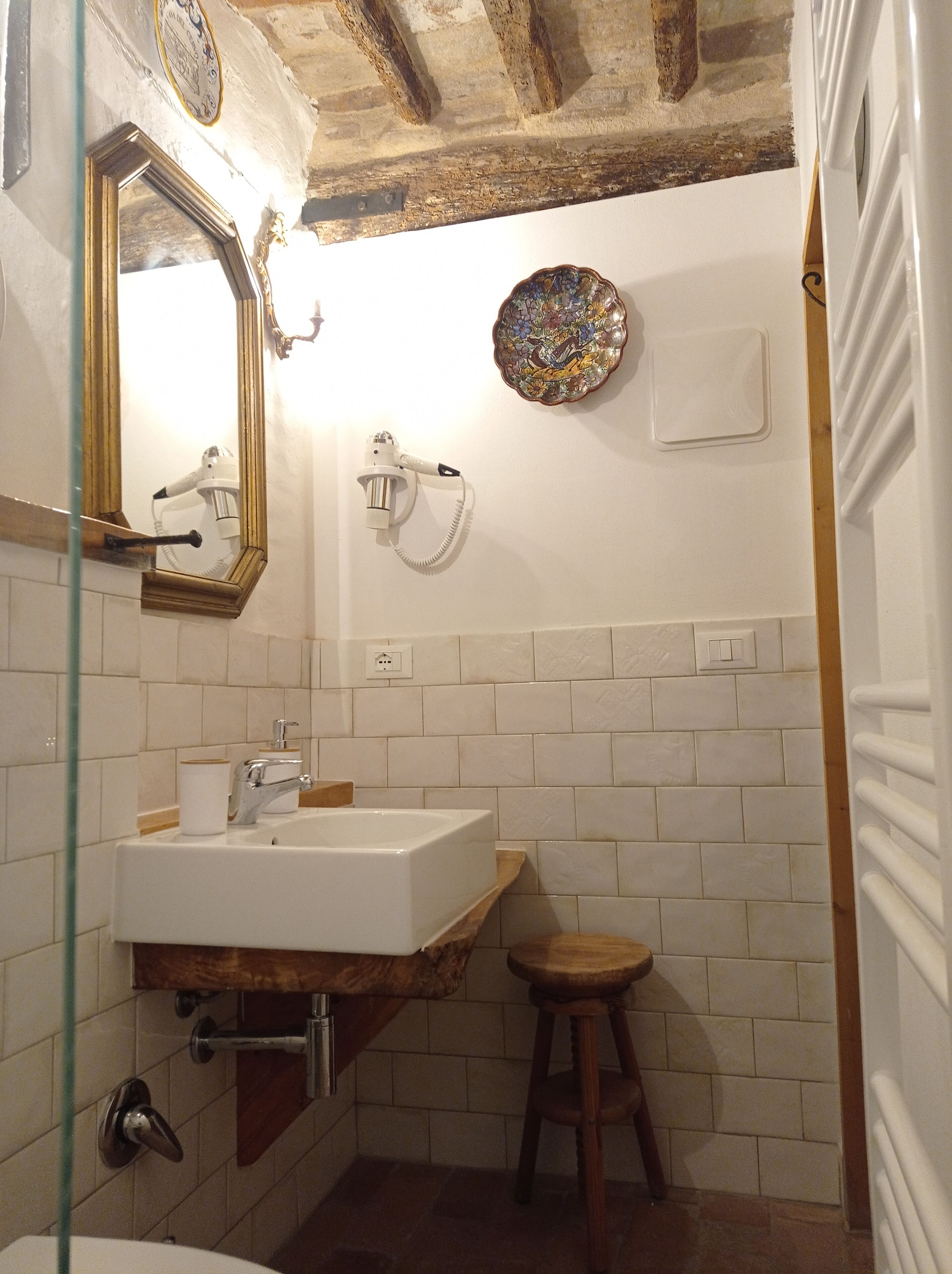 A bathroom with a white sink, a wooden stool, a mirror, a hairdryer, and a decorative plate on the wall.