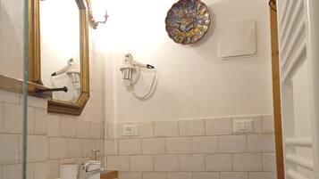 Ein Badezimmer mit einem weißen Waschbecken, einem hölzernen Hocker, einem Spiegel, einem Föhn und einer dekorativen Platte an der Wand.