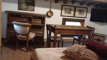 Una habitación rústica con vigas de madera a la vista, un escritorio de madera, una silla, una cama con almohada estampada y un televisor en la pared.