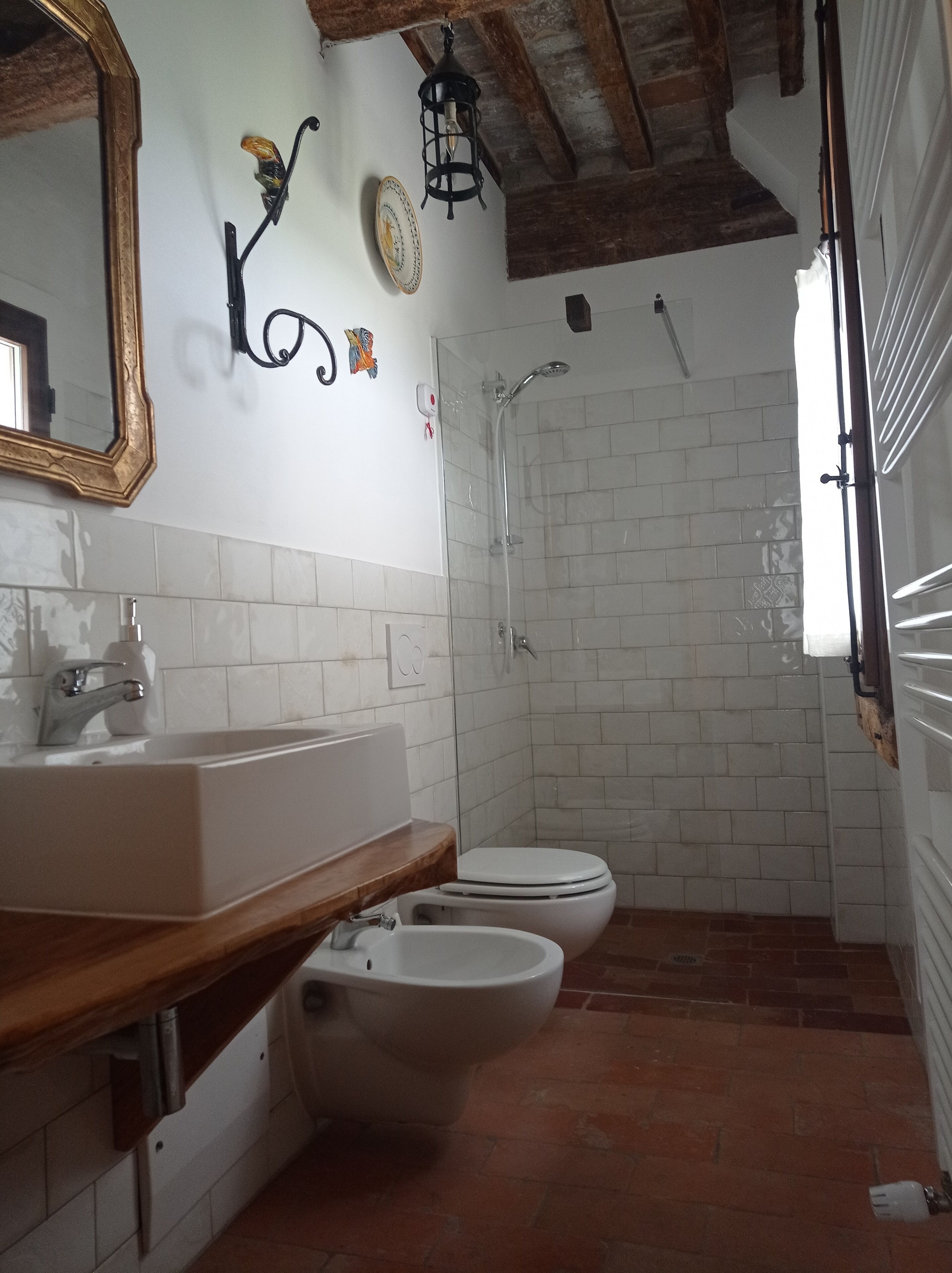 Ein Badezimmer mit einem weißen Waschbecken, einer Toilette, einem Bidet, einer Dusche und einem Spiegel mit dekorativem Rahmen.