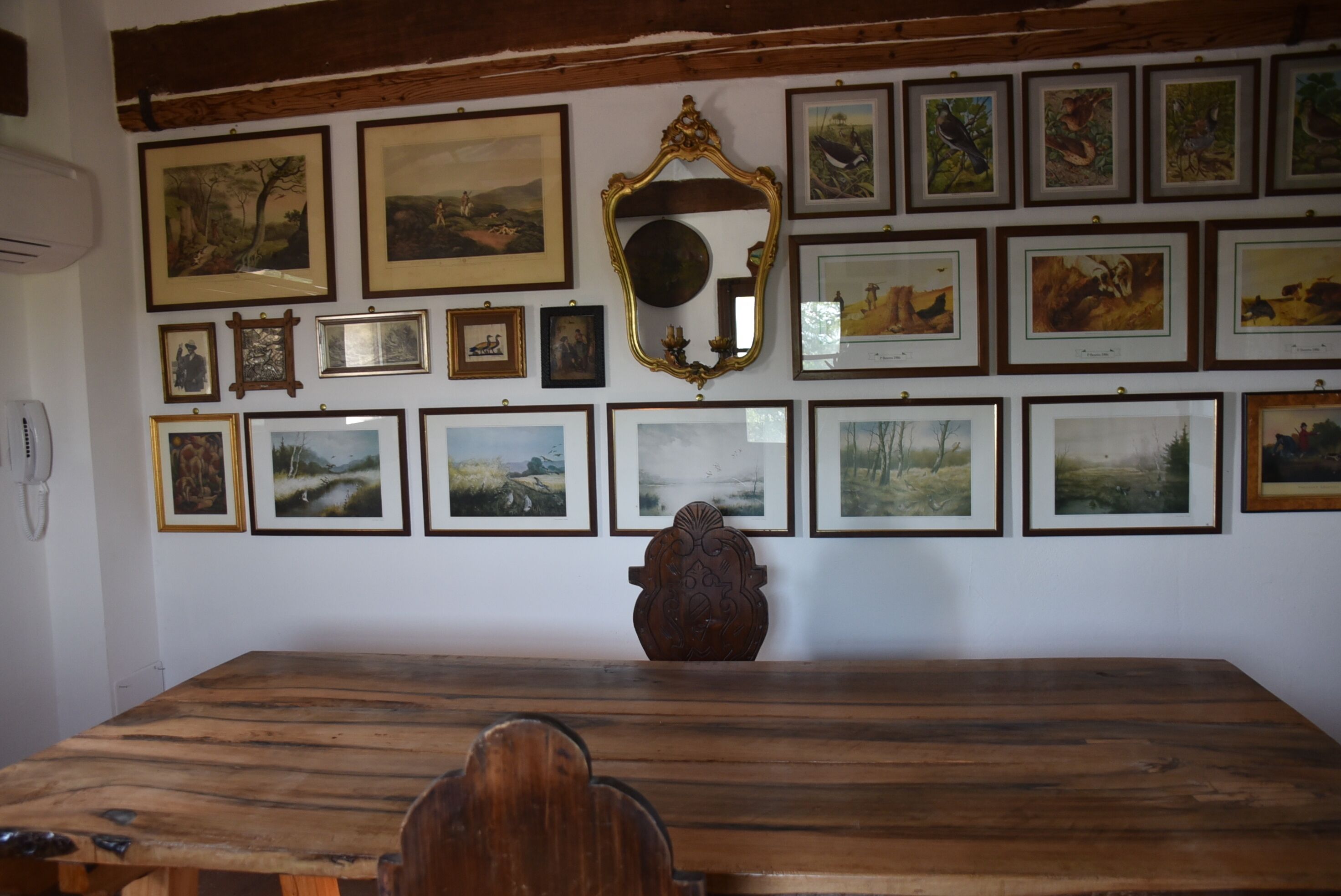A dining area with a wooden table and chairs, surrounded by framed pictures on the wall.