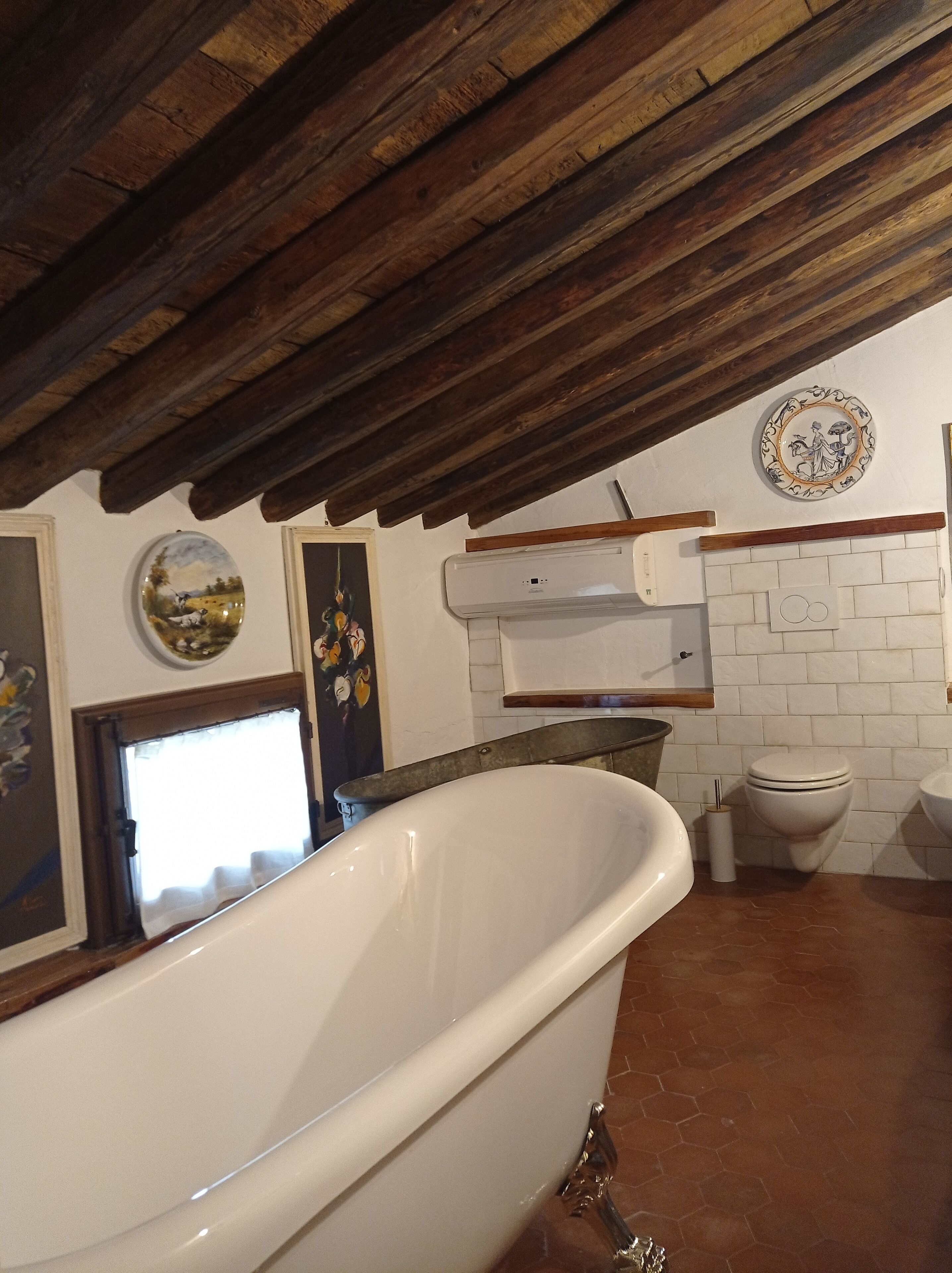 A bathroom with a freestanding bathtub, a white toilet, and a wall-mounted air conditioning unit.