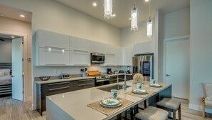 A modern kitchen with white cabinets, stainless steel appliances, and a central island with bar stools. - NEW - Heated Pool & Spa - Lake - Western Exposure (Cape Coral)