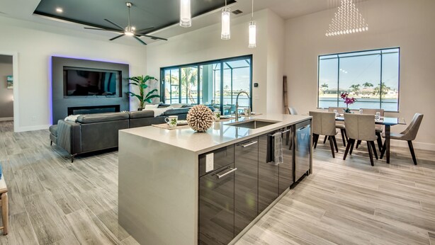 A modern kitchen with a central island, a dining area with a large window, and a living room with a TV and seating. - NEW - Heated Pool & Spa - Lake - Western Exposure (Cape Coral)