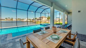 A dining area with a view of a swimming pool and a clear sky. - NEW - Heated Pool & Spa - Lake - Western Exposure (Cape Coral)