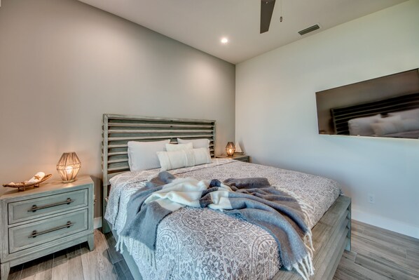 A modern bedroom with a large bed, a nightstand with a lamp, and a wall-mounted TV.