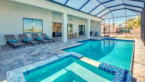A swimming pool with tiled edges, lounge chairs, and a covered patio area. - NEW - Heated Pool & Spa - Lake - Western Exposure (Cape Coral)