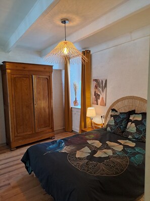 A bedroom with a bed, a wooden wardrobe, a hanging lamp, and a wall painting.