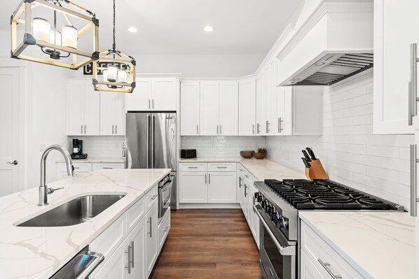 A modern kitchen with white cabinets, a stainless steel sink, a gas stove, and a wooden floor.