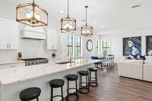 A modern kitchen with white cabinets, a large island with stools, and pendant lighting.
