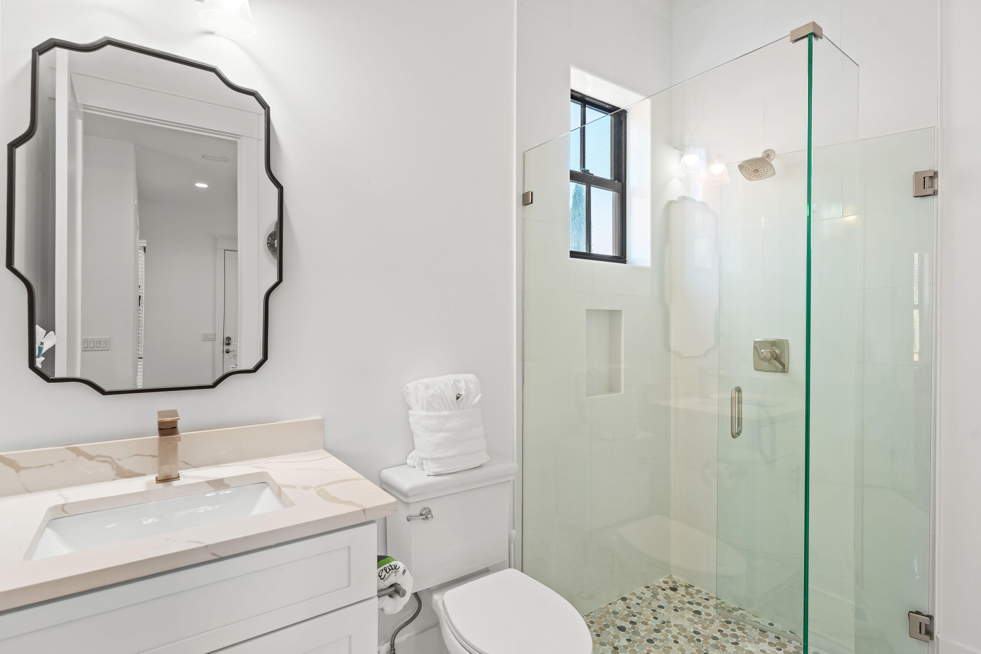 Une salle de bain moderne avec une douche à parois de verre, un grand miroir et un lavabo en marbre.