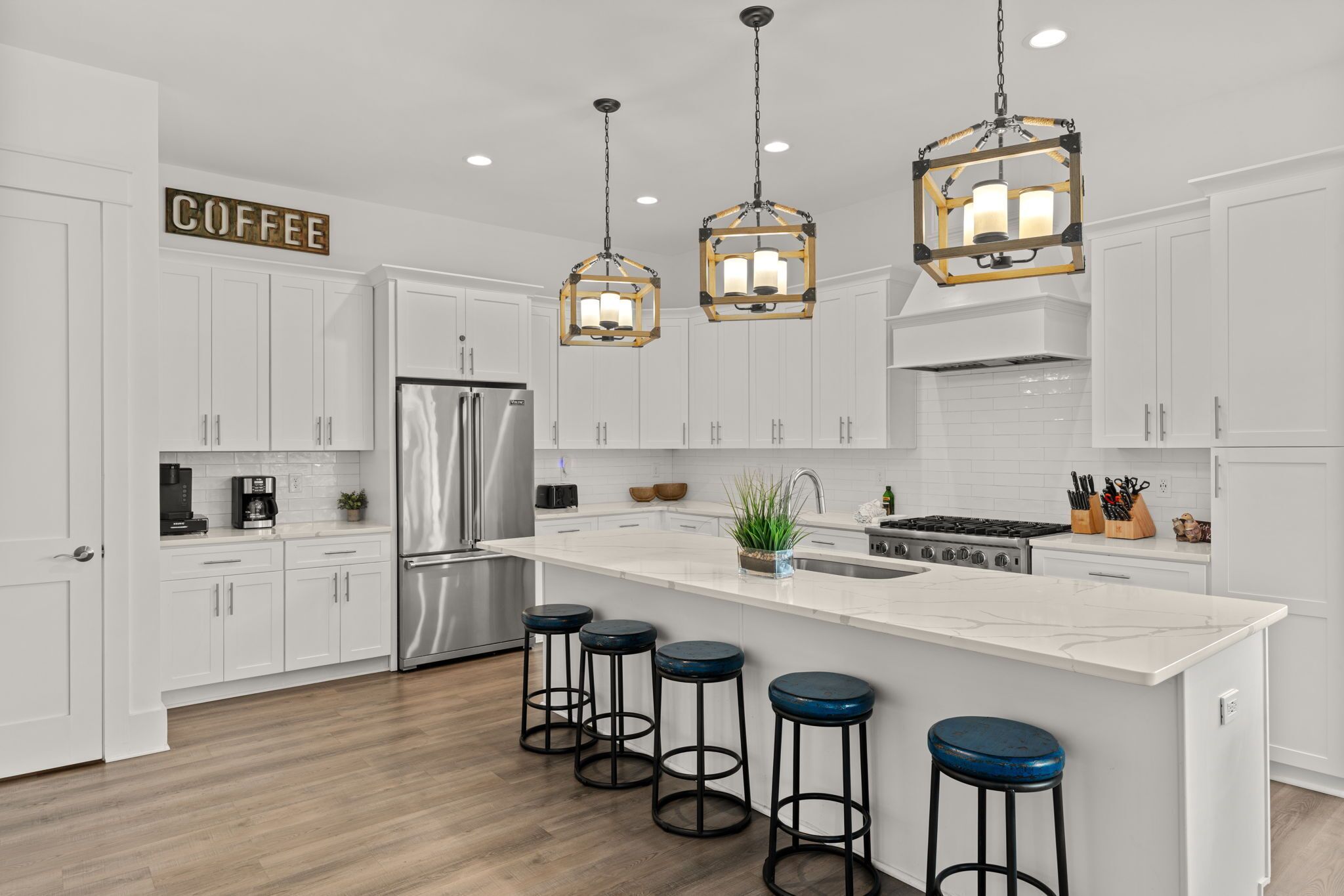 A modern kitchen with white cabinets, stainless steel appliances, a central island with stools, and hanging pendant lights.
