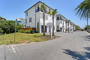 A two-story residential building with a flat roof, a balcony on the second floor, and a front yard with palm trees. - Brand New Luxury home, Free Beach Chair Service, Private Pool, Perfect Location (Santa Rosa Beach)