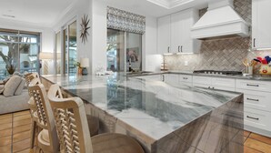 Une cuisine moderne avec des meubles blancs, un grand îlot en marbre et un dosseret de carreaux disposés en motif chevrons.