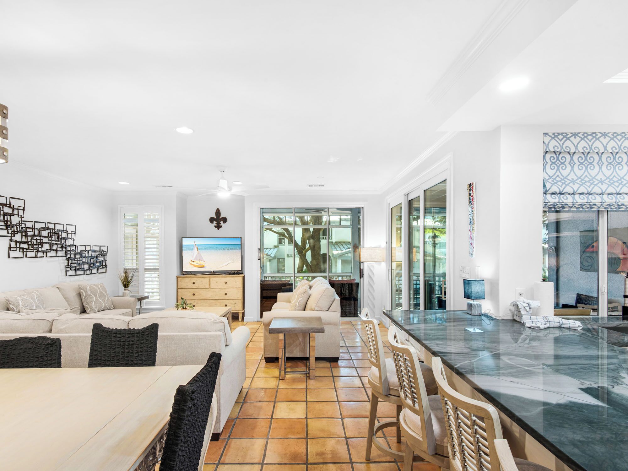 Uma sala de estar moderna com sofá, mesa de jantar e cadeiras. Há uma TV sobre um móvel de madeira, e uma janela grande com vista para o exterior.