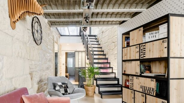 Una sala de estar moderna con una escalera, una estantería y una zona de estar acogedora.