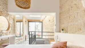 Un dormitorio con cama, mesita de noche, lámpara colgante, pared de piedra y vistas al exterior.
