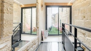 Un interior moderno con paredes de piedra, grandes puertas correderas de cristal que dan a un espacio exterior y una barandilla metálica.