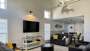 Un salon moderne doté d’un téléviseur à écran plat, de canapés gris, d’une table basse et d’un coin repas avec une table et des chaises.
