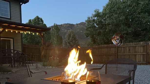 Une terrasse extérieure avec un foyer, deux verres de vin rouge et une clôture en bois en arrière-plan.