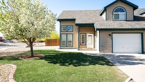 Une maison à deux étages avec un garage, une porte d’entrée et un arbre dans le jardin.
