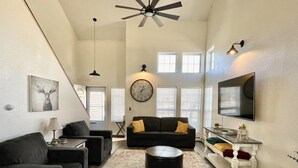 Un vaste salon doté d’un ventilateur de plafond, d’une grande horloge murale et d’un téléviseur à écran plat fixé au mur.