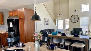 Une cuisine moderne avec des meubles en bois, un réfrigérateur noir et un coin repas doté d’une table en bois, mise pour quatre personnes.