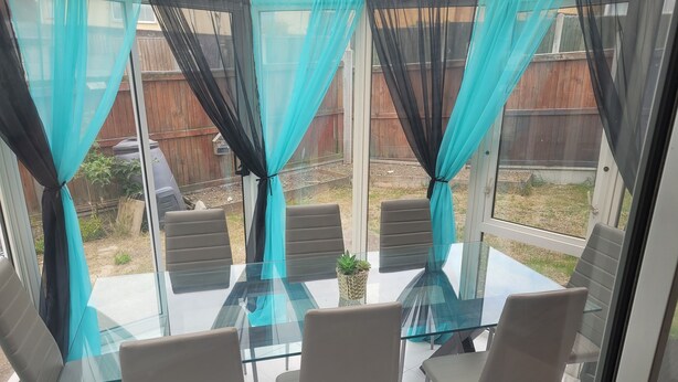 A glass table with four chairs in a sunroom with curtains. - Beautiful 3-bed House in Ramsgate (Ramsgate)