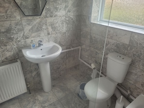 Un baño con un lavamanos pedestal blanco, un inodoro y un radiador.