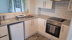A compact kitchen with white cabinets, a built-in oven, a dishwasher, and a tiled backsplash. - Beautiful 3-bed House in Ramsgate (Ramsgate)