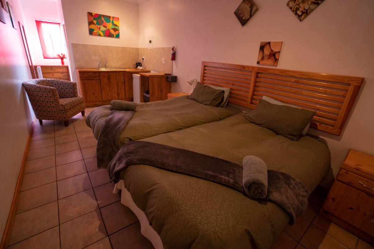 A bedroom with a large bed, a wooden headboard, a chair, and a small wooden cabinet.