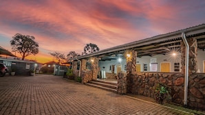 A hotel entrance with stone pillars, a covered walkway, and a sunset sky.