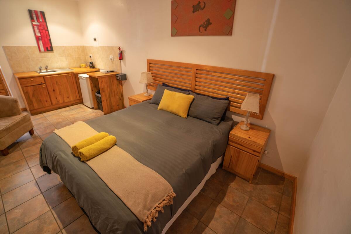 A bedroom with a large bed, wooden headboard, bedside tables, a nightstand, a small wooden cabinet, and a bathroom with a sink and toilet.