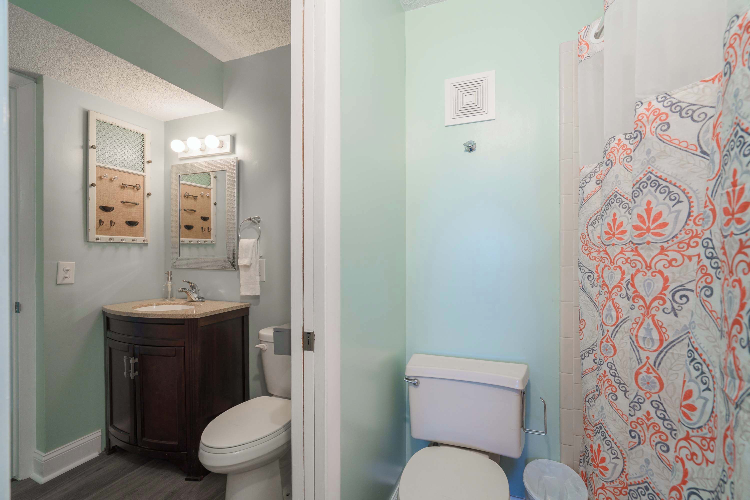 A bathroom with a vanity, two toilets, and a shower curtain.