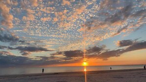 Ein Strand bei Sonnenuntergang, Menschen flanieren, und ein klarer Himmel.