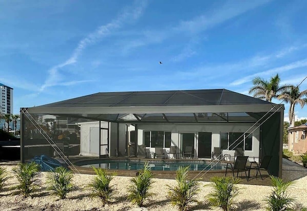 A modern house with a glass-enclosed patio, a pool, and outdoor seating.
