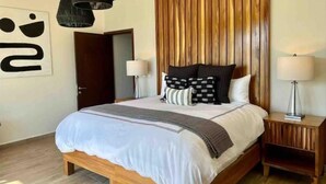 Ein modernes Schlafzimmer mit einem Holzkopfteil, einem großen Bett mit weißer Bettwäsche, zwei Nachttischlampen und einem Nachttisch aus Holz.