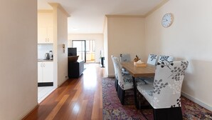 A dining area with a wooden table and floral-patterned chairs, a clock on the wall, and a view into the kitchen. - Sydney Two-Level 3BDR 3BATH near CBD & Olympic Park  (Burwood)